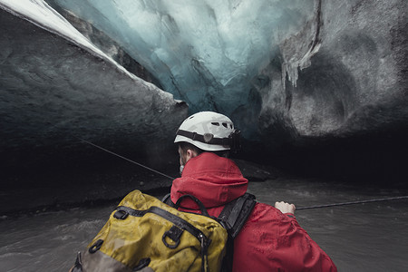 冰川运动摄影照片_冰岛瓦特纳约库尔国家公园瓦特纳约库尔冰川冰洞中一名男子用绳子过河