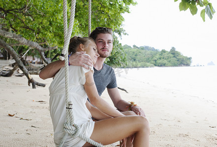 一对年轻夫妇坐在泰国克拉丹的海滩秋千上