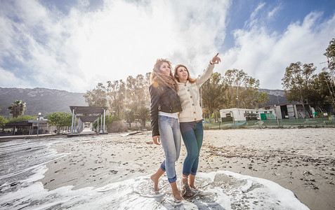 两个年轻的女性朋友赤脚在海滩上散步