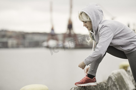 运动裤女摄影照片_女跑步者在码头上系教练鞋带