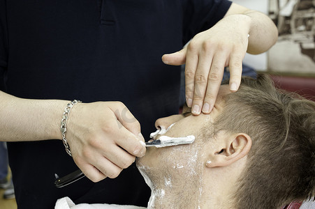 儿童理发摄影照片_理发店里拿着直剃刀给顾客刮胡子的年轻人的剪裁