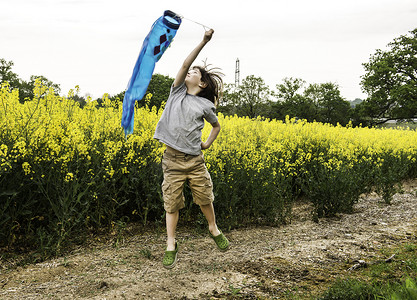 男孩在黄色花田小径上拉着鱼风筝跳跃