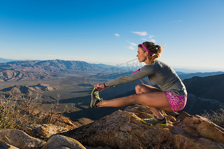 动物脚趾摄影照片_美国加利福尼亚州松树谷太平洋山脊步道年轻女性跑步者蹲着触摸脚趾的背影