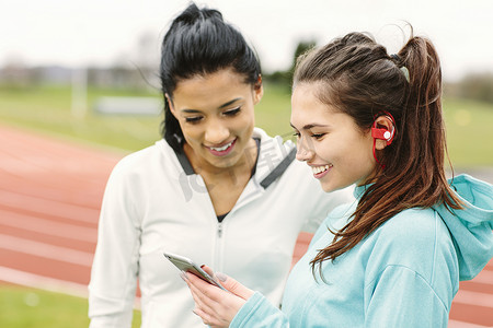 两名年轻女子在跑道旁看着智能手机