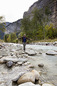 一名男性徒步旅行者跨过河中的岩石格林德尔瓦尔德瑞士