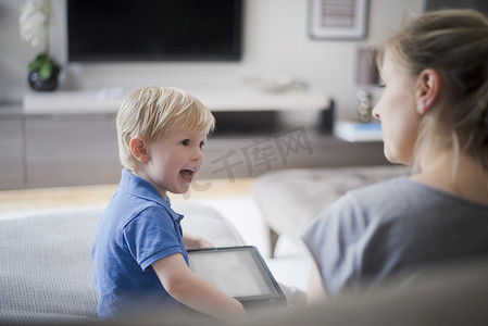 母子沟通摄影照片_母子俩坐在一起儿子拿着数字平板电脑笑着
