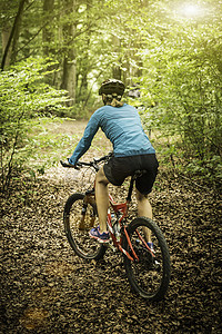 成年女性山地自行车手在森林小径上骑行的后视线