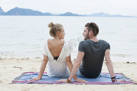一对年轻夫妇坐在泰国克拉丹的海滩上