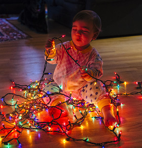 蹒跚学步的女孩子在地板上玩五颜六色的圣诞彩灯