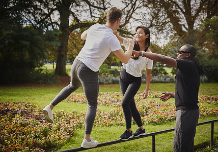 男运动裤摄影照片_一男一女和私人教练在公园的栅栏上保持平衡