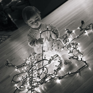 儿童baby摄影照片_蹒跚学步的女孩在地板上玩圣诞彩灯的