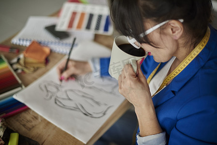 设计工作室里的女人喝着咖啡画着时尚设计的素描