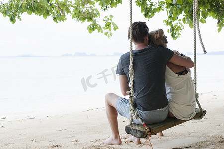 坐在沙滩秋千上的年轻夫妇的背影泰国克拉丹