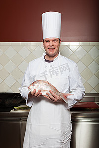 安康鱼摄影照片_男厨师在商业厨房里端着鱼