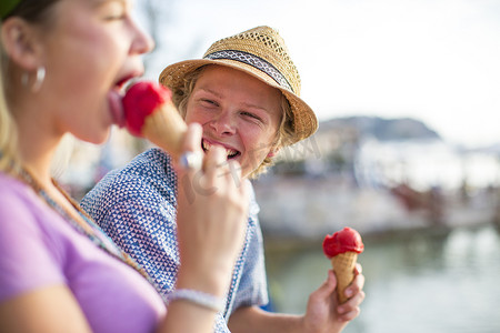 西班牙马略卡岛一对年轻夫妇在海滨边笑着吃着蛋卷冰淇淋