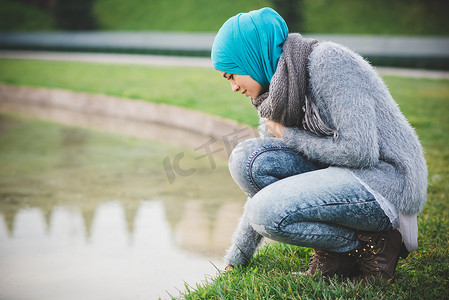 戴着头巾的年轻女子蹲在公园湖边