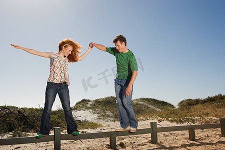 享受旅行摄影照片_一名年轻男子帮助一名女子在栅栏上保持平衡