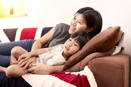 年轻的中国母女俩在家一起躺在沙发上看电视