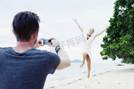年轻男子在拍摄女友在海滩上跳跃泰国克拉丹