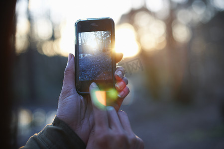 暮光森林摄影照片_在智能手机上拍摄森林的女人的手