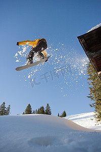 至低摄影照片_一名滑雪板运动员从小屋屋顶跳下