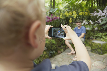 新加坡植物园男孩在智能手机上给父亲拍照的背影