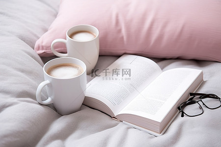 枕头上放着两个咖啡杯和一本打开的书