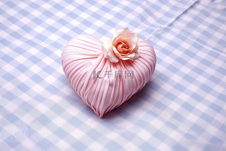 一朵心形的粉红色花朵坐落在白色格子桌布上