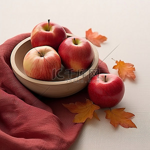 四个红苹果放在一个小碗里，放在铺满秋叶的桌子上