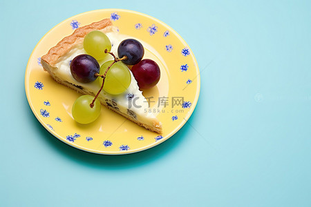 黄色背景上蓝色盘子上的一片披萨，上面有樱桃和葡萄