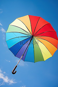 彩虹蓝天背景图片_天空中撑着一把彩虹伞，映衬着蓝天