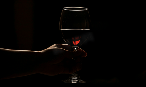 在黑暗中握着酒杯的女性的手