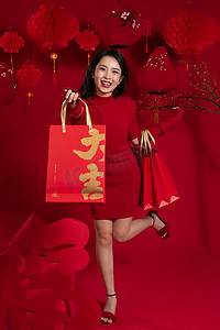 年货背景摄影照片_新年购物红色背景下的一位亚洲青年女性拿着购物袋