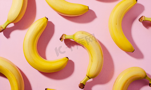 黄色风格摄影照片_粉红色背景上鲜黄香蕉的彩色水果图案从顶部看