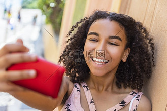 美丽的愉快的混合种族非洲裔美国人女孩青少年女性孩子微笑与完美的牙齿采取selfie照片与手机