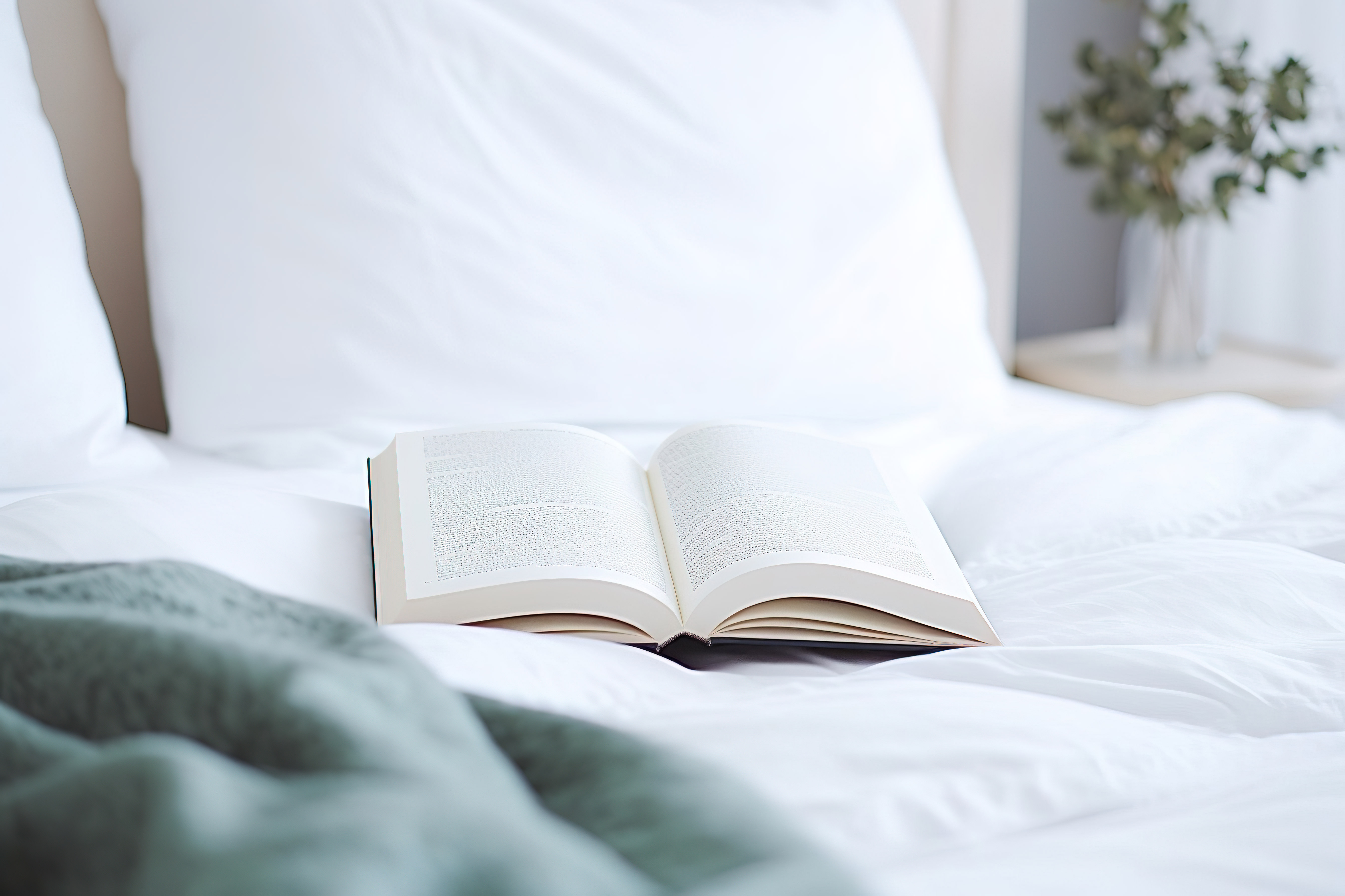 一本书放在一张带枕头的白色床上图片