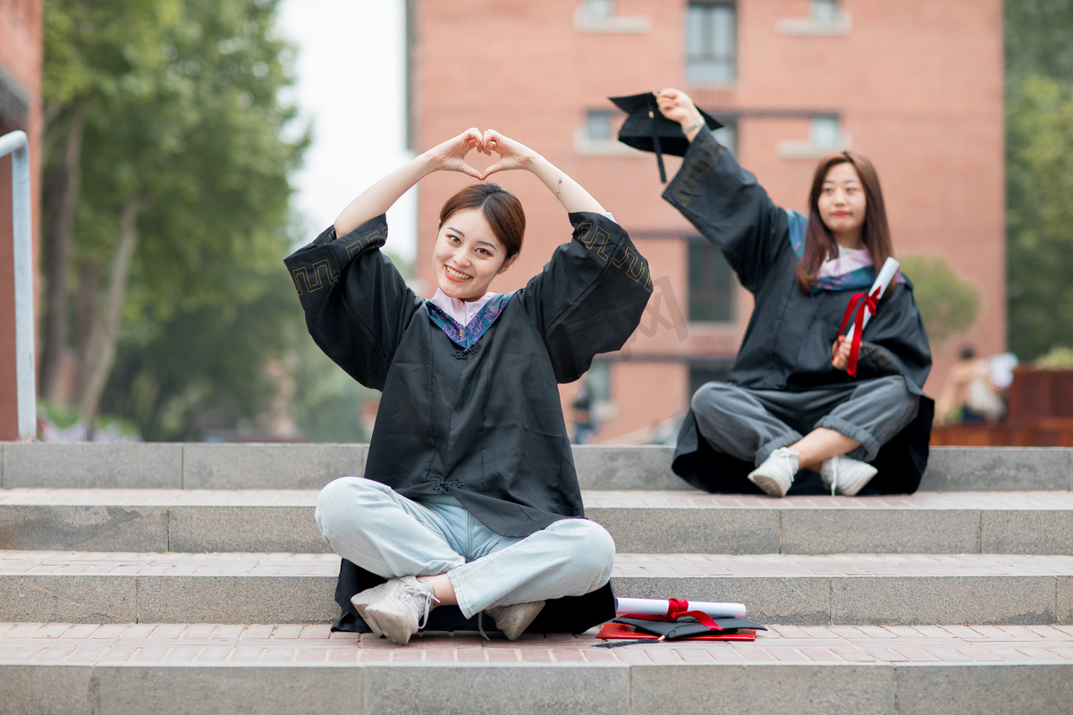 毕业季白天穿着学士服的美女毕业生户外比心摄影图配图图片