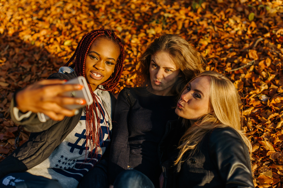 三个漂亮的女性在秋天公园自拍照。与不同的有色皮肤的可爱女孩。女性躺在树叶，在相机做鬼脸笑道。Autamn 阳光明媚的一天图片