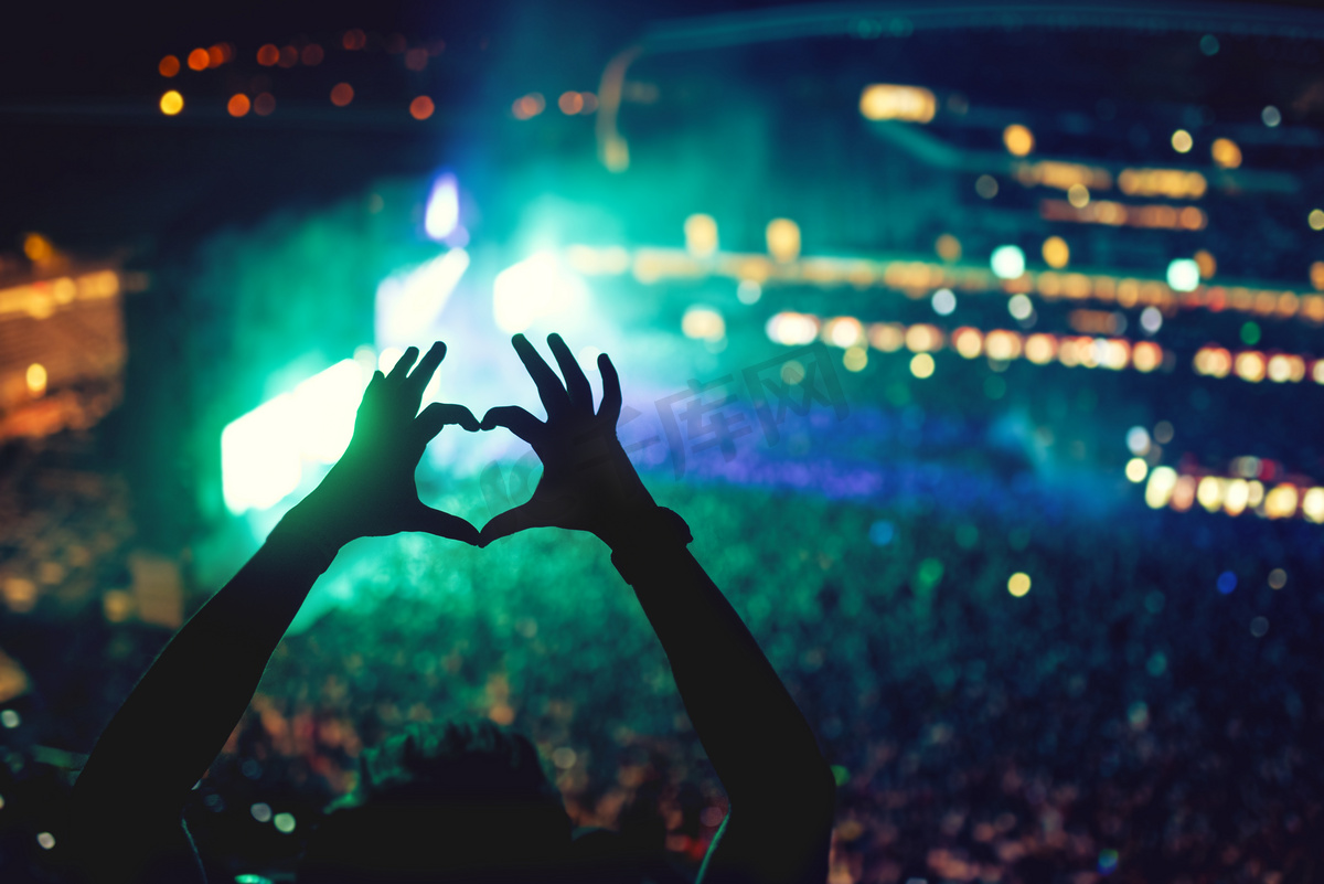 音乐会上，爱艺术家和节手的心形。音乐演唱会与灯和一个男人享受这场音乐会的轮廓图片