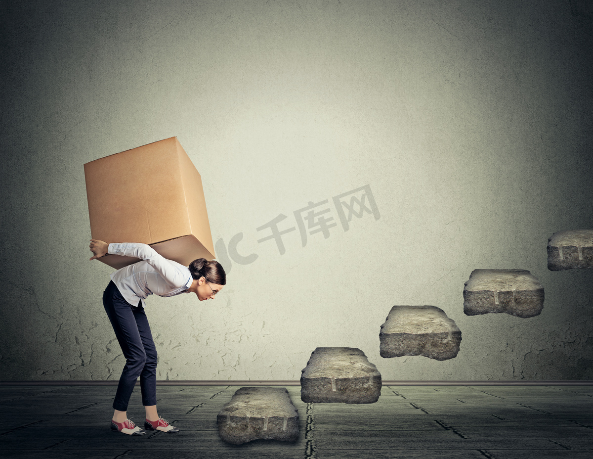 Difficult task concept. Young woman carrying heavy box upstairs图片