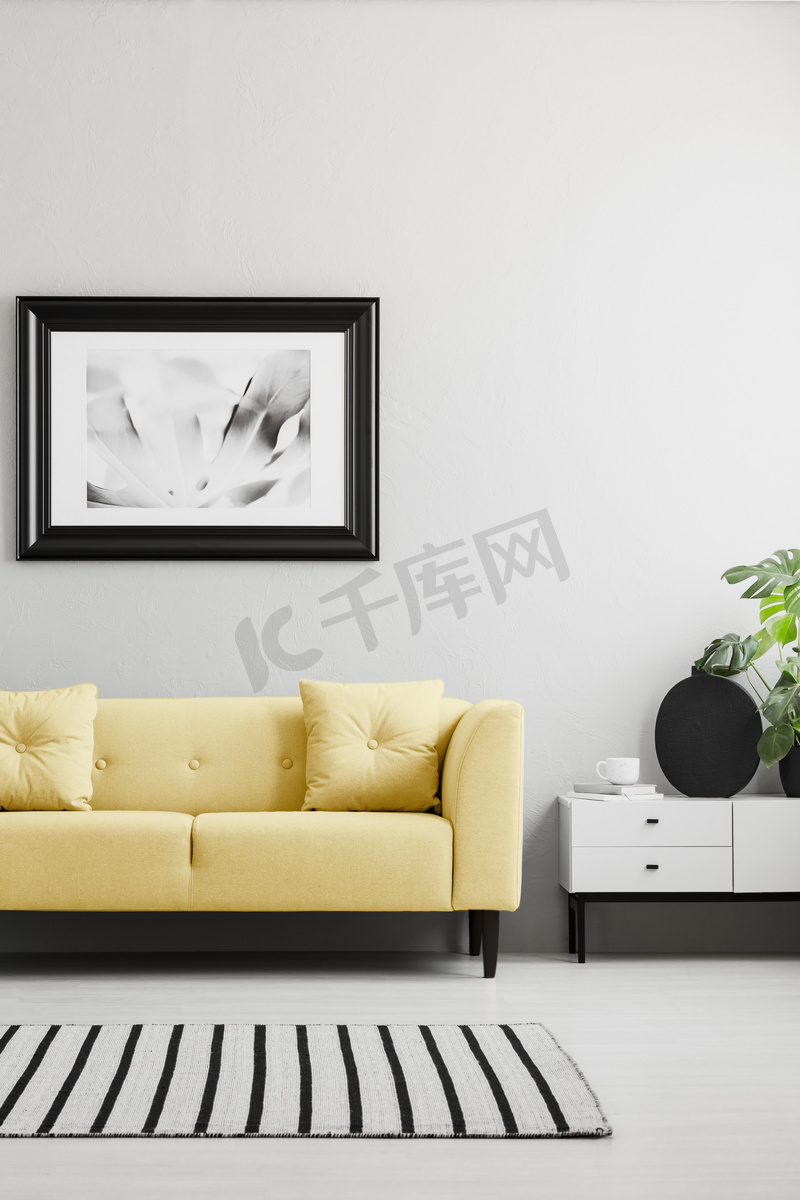 海报上面的黄色沙发在最小的灰色客厅内部与地毯和橱柜。真实照片图片