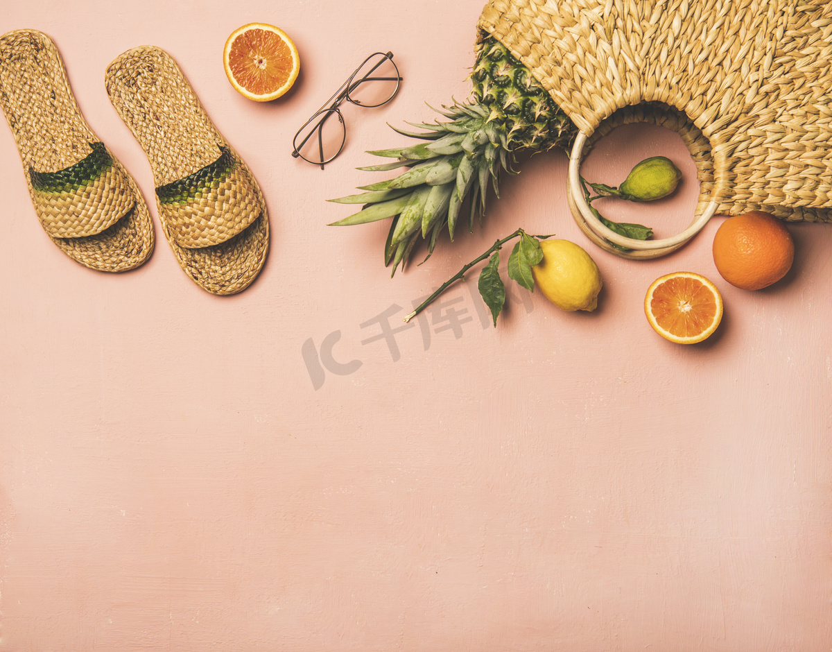 夏季服装项目。平铺的夏季拖鞋，太阳镜，柳条袋和新鲜水果在柔和的粉红色背景，顶视图，复制空间。夏季海滩度假理念图片