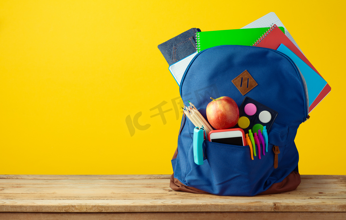 带笔记本、智能电话和铅笔的书包背包, 上面有黄色背景.图片