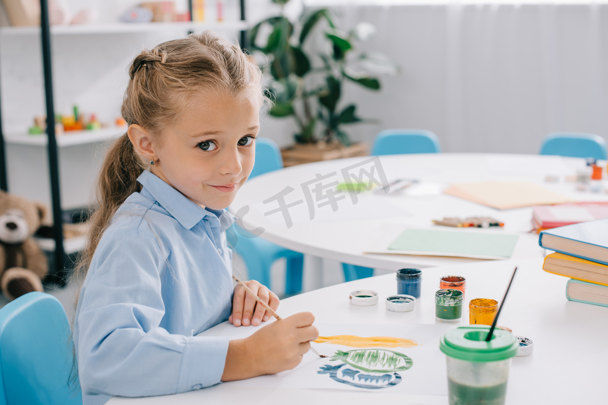 可爱的孩子坐在桌子上, 油漆和油漆刷的侧面视图 图片