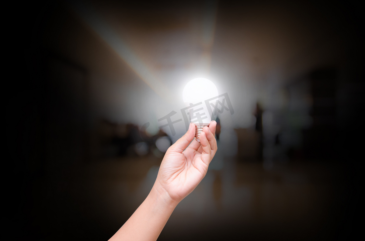 女人手上握有上模糊室内大厅的办公室照明 Led 灯泡图片