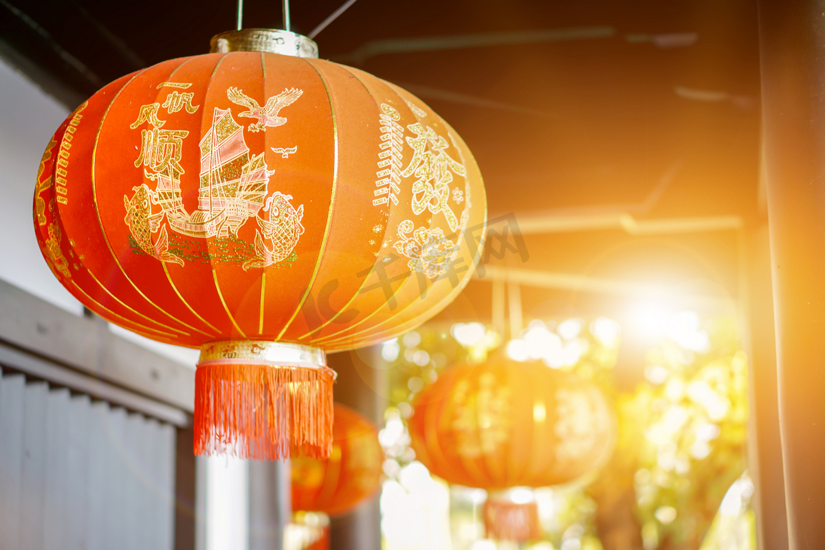 美丽的中国装饰红色灯笼挂在古寺天花板上，背景模糊不清，阳光灿烂。 2.中文灯笼上的字母在英语中是吉祥的恭维话.图片