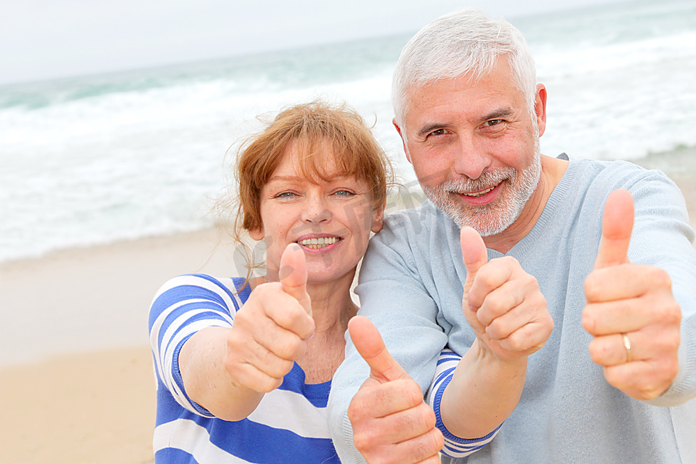 快乐的高年级夫妇在海滩竖起大拇指图片