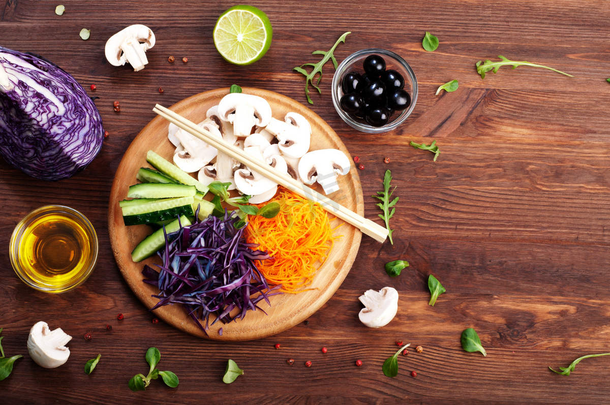 The concept of dietetic vegetarian food. Bright juicy shredded vegetables, such as carrots, purple cabbage, mushrooms and cucumbers, which lies on a circular wooden cutting board. Natural organic products, ready to eat图片