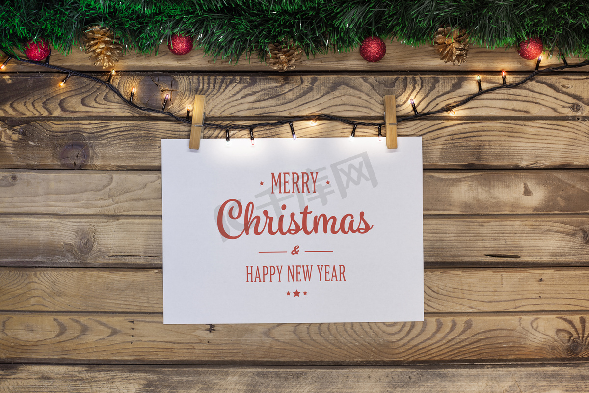 圣诞问候在一个白色的床单上挂着一个花环与 clothespins 在一个木质的背景上装饰绿色的金属丝和红色的玩具图片