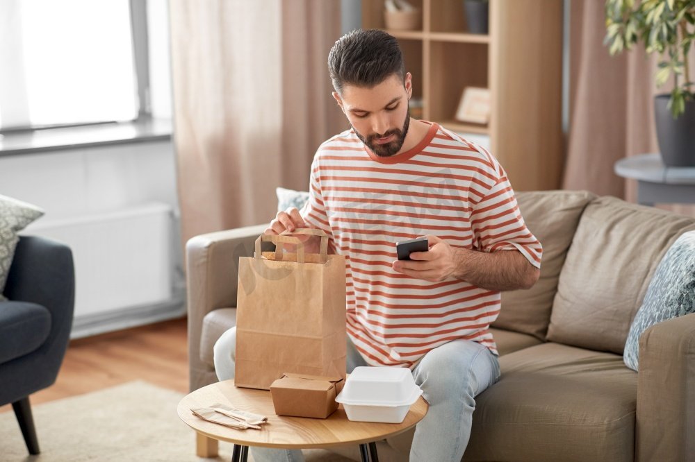 沟通、休闲和人的概念-男人在家里用智能手机叫外卖点餐。一名男子在家里用手机查看订餐情况图片